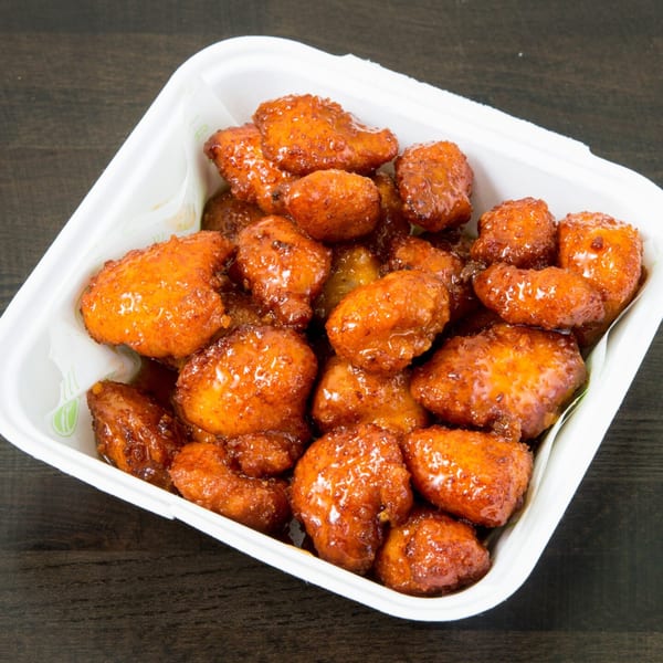 A white takeout container filled with glistening, orange-brown boneless chicken wings in sauce.
