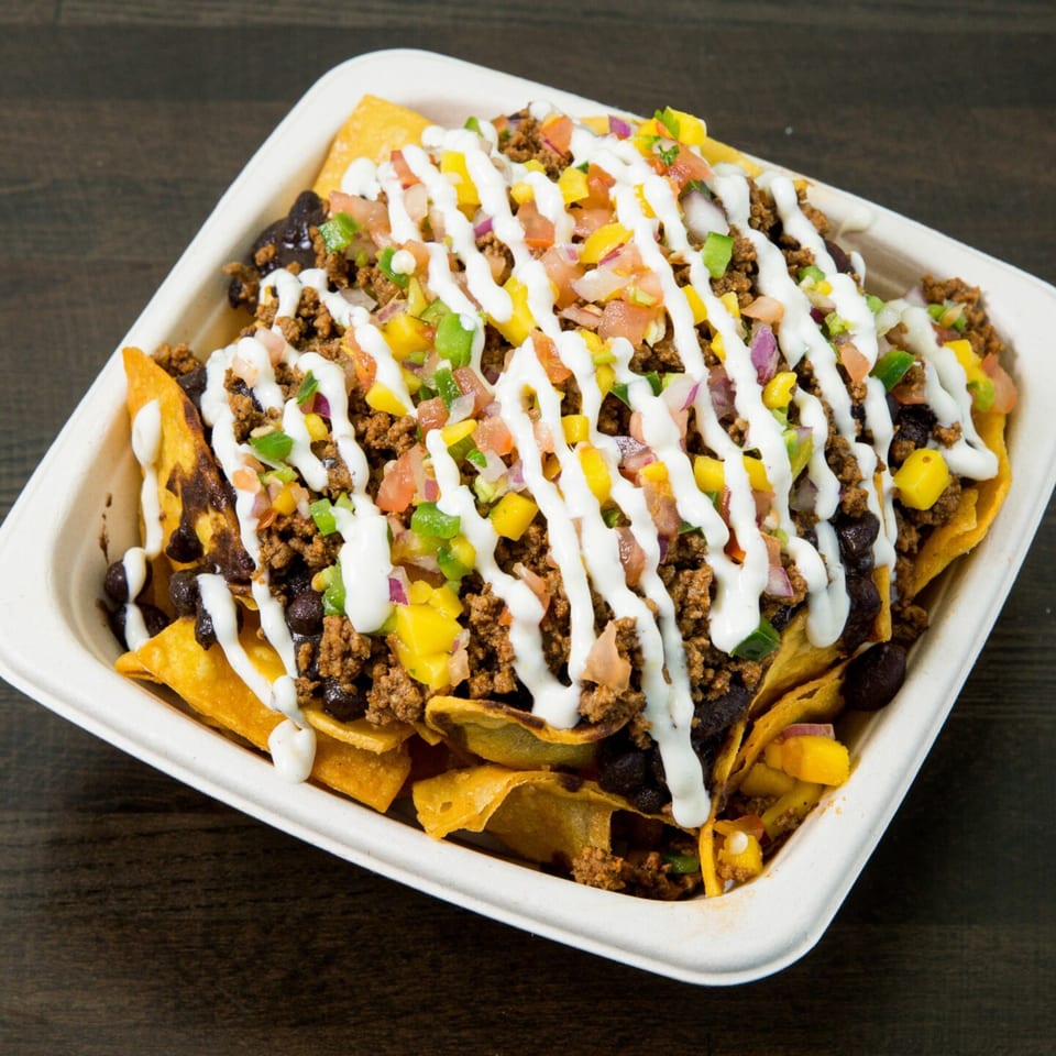 Nachos with ground beef, black beans, corn, pico de gallo, and a drizzle of white sauce.