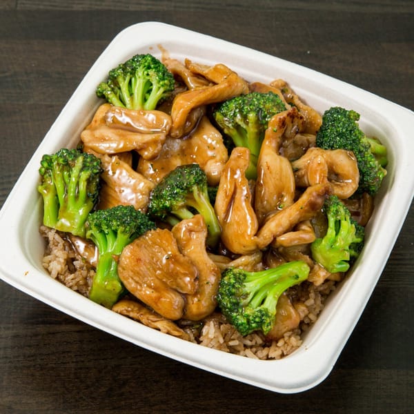 Chicken and broccoli stir-fry with brown rice in a white takeout container on a dark wooden table.