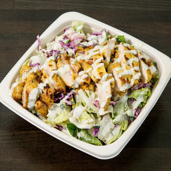 Grilled chicken salad with lettuce, red cabbage, and white dressing in a white container.