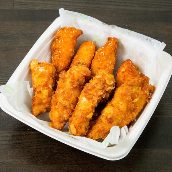 Crispy fried chicken tenders, some topped with sesame seeds, in a white paper container.